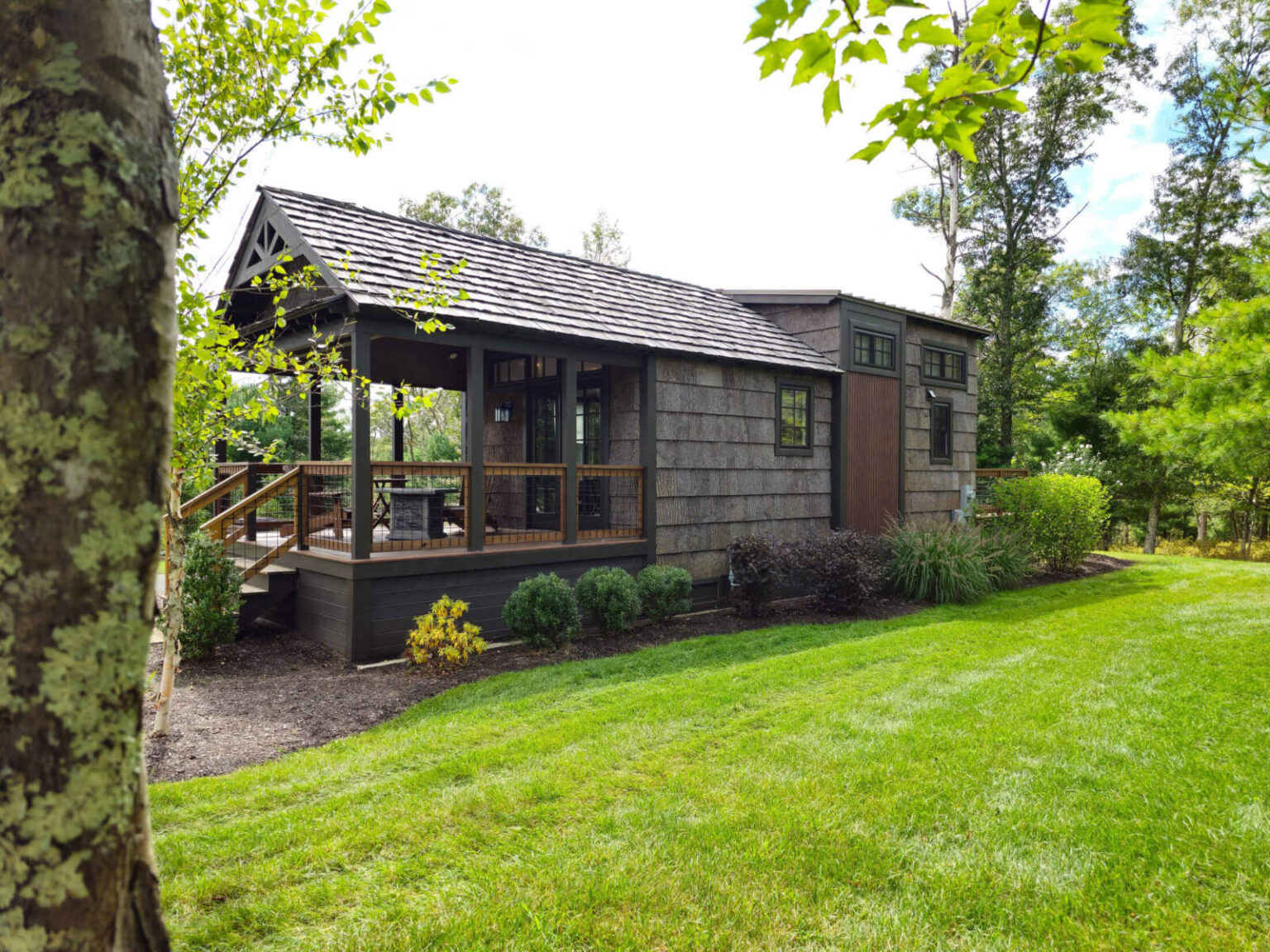 Rustic tiny home with a large front porch in a lush green setting